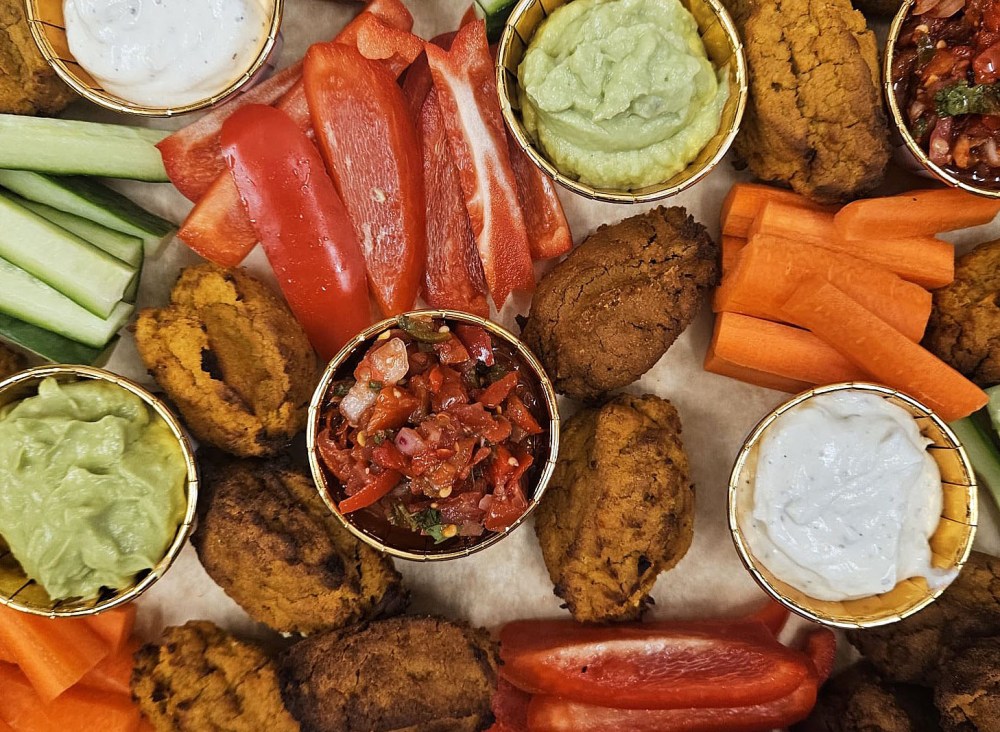 An image showing a sweet potato falafel platter including falafels, dips, carrot sticks, cucumber and sticks of red pepper
